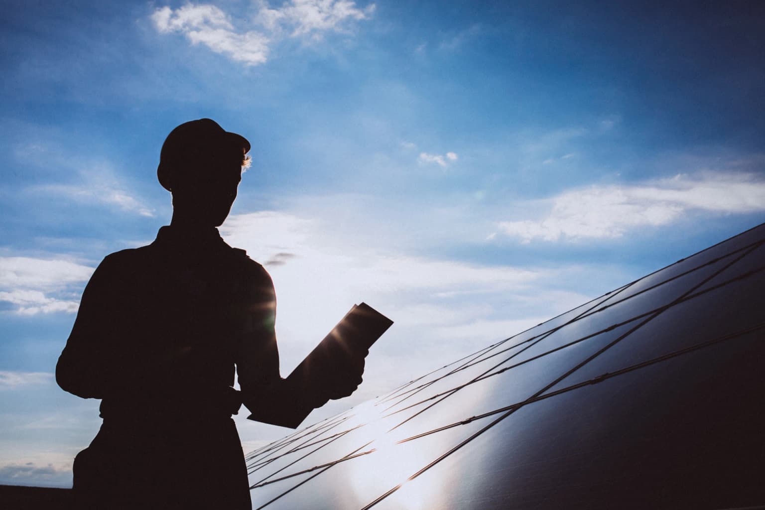 Silhouette d'un électricien sur toiture solaire au coucher du soleil, tablette en main, Be'energies sur le terrain