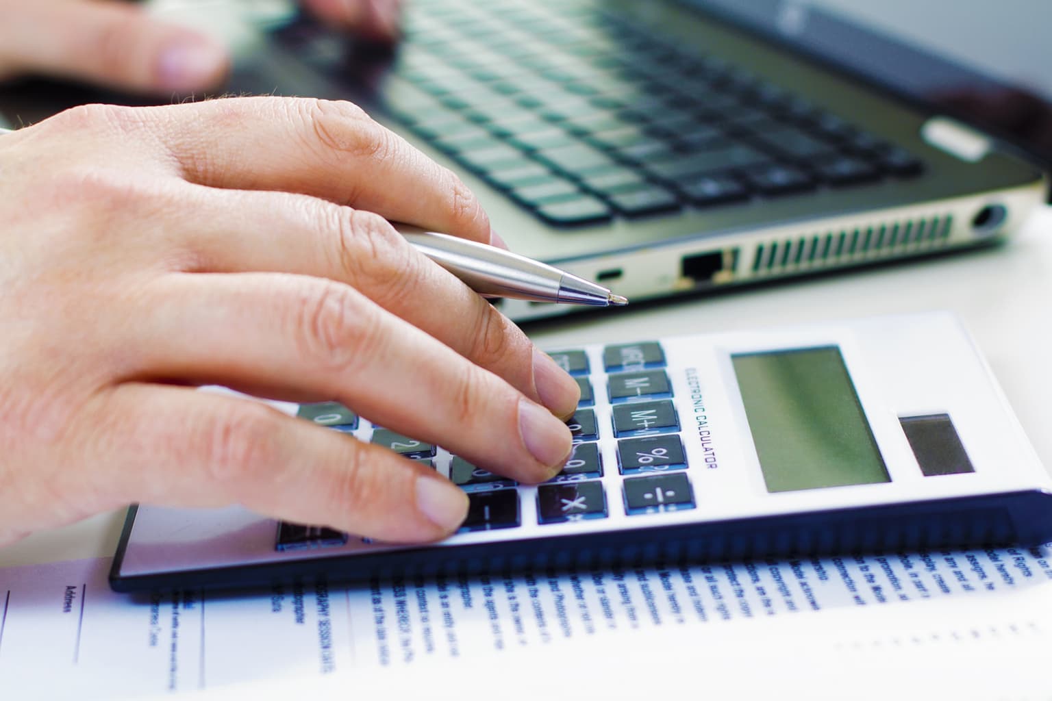 Main qui tape sur une calculatrice à côté d'un ordinateur, calcul de devis